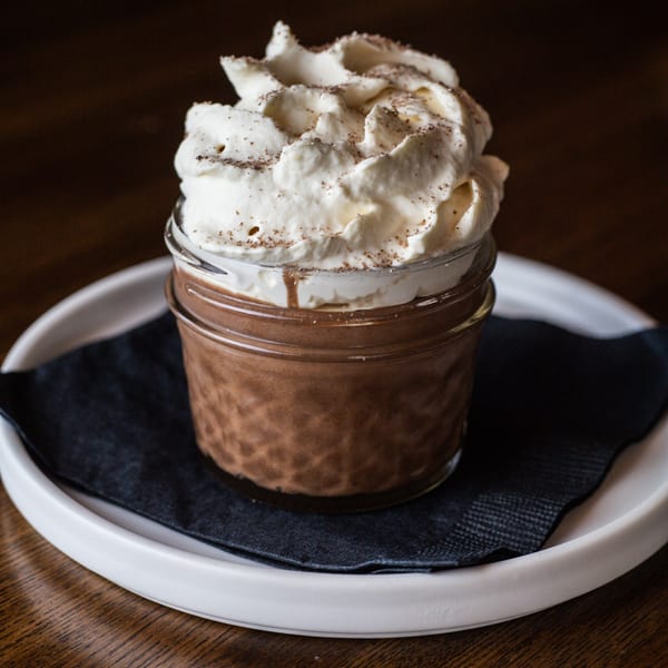 Chocolate dessert in a glass jar, topped with whipped cream and a sprinkle of cinnamon.