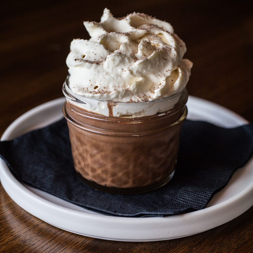 Chocolate dessert in a glass jar, topped with whipped cream and a sprinkle of cinnamon.
