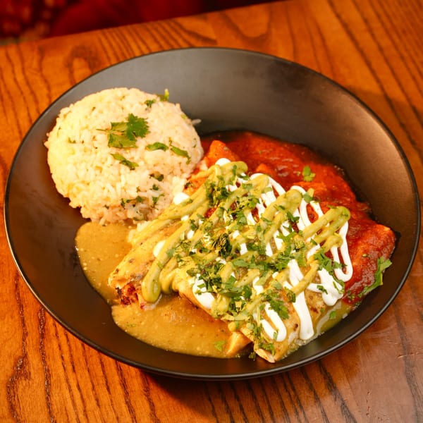 Mesa Latin Kitchen's enchiladas with red and green sauce, rice, and cilantro on a black plate.