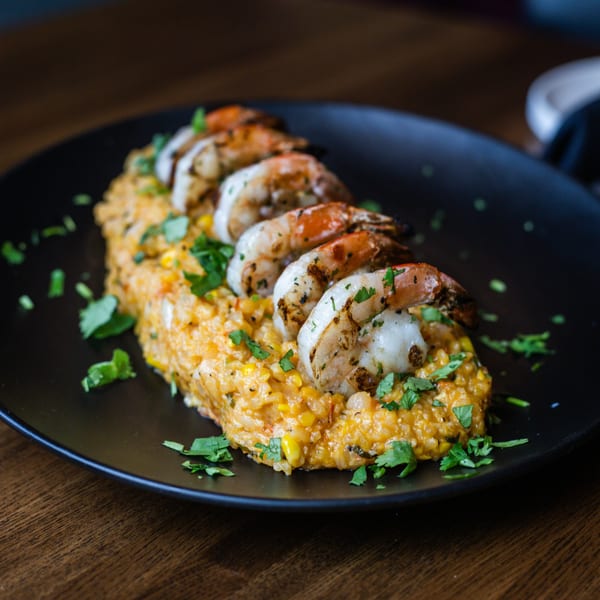 Grilled shrimp on a bed of yellow rice and corn, garnished with fresh cilantro on a black plate.